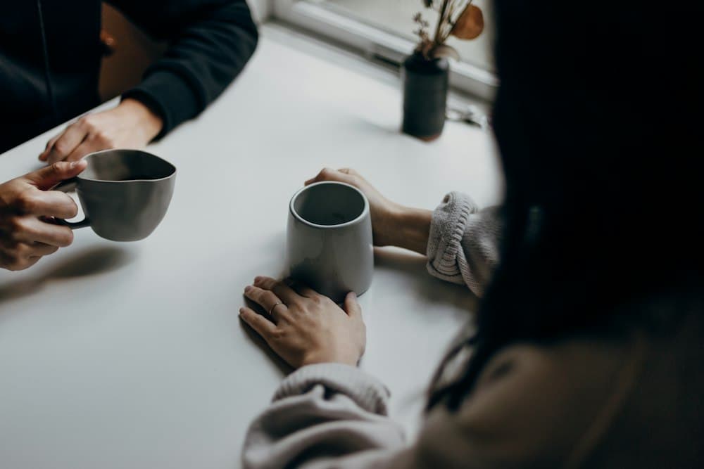 Duas pessoas conversando à mesa, cada uma segurando uma caneca
